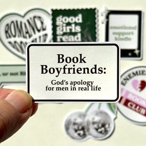 Pode incluir: Um autocolante retangular com fundo branco e contorno preto. O texto diz: Book Boyfriends: God's apology for men in real life. O autocolante está rodeado por outros autocolantes com vários designs e textos relacionados com livros.