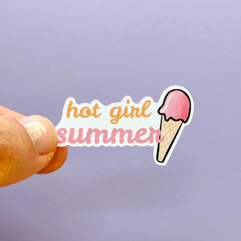May include: A die-cut sticker featuring the text hot girl summer in orange and pink cursive lettering, accompanied by a graphic of a pink ice cream scoop on a tan waffle cone, all outlined in white against a solid light purple background.