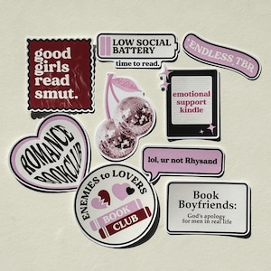 Könnte beinhalten: Eine Sammlung von Vinyl-Aufklebern mit buchbezogenen Motiven in Rosa-, Kastanienbraun- und Schwarztönen. Der Text umfasst "good girls read smut", "LOW SOCIAL BATTERY", "ENDLESS TBR", "emotional support kindle", "lol, ur not Rhysand" und "Book Boyfriends".