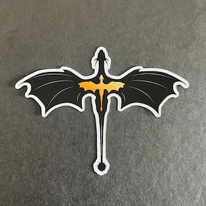Peut inclure: Un autocollant d&eacute;coup&eacute; repr&eacute;sentant la silhouette d'un dragon noir aux ailes largement d&eacute;ploy&eacute;es. Un graphisme plus petit de dragon jaune orang&eacute; vif est centr&eacute; sur le corps noir. Le motif pr&eacute;sente une longue queue avec une pointe &eacute;pineuse.