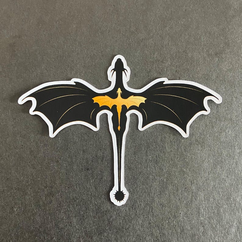 Peut inclure: Un autocollant d&eacute;coup&eacute; repr&eacute;sentant la silhouette d'un dragon noir aux ailes largement d&eacute;ploy&eacute;es. Un graphisme plus petit de dragon jaune orang&eacute; vif est centr&eacute; sur le corps noir. Le motif pr&eacute;sente une longue queue avec une pointe &eacute;pineuse.