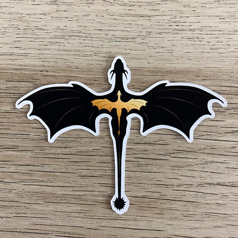 Peut inclure: Un autocollant d&eacute;coup&eacute; repr&eacute;sentant la silhouette noire d'un dragon aux grandes ailes d&eacute;ploy&eacute;es et &agrave; la longue queue termin&eacute;e par une nageoire &eacute;pineuse. Au centre du dos du dragon se trouve un petit motif de dragon dor&eacute; aux ailes d&eacute;ploy&eacute;es.