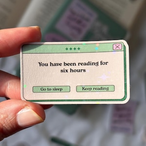 Może przedstawiać: Prostokątna naklejka z zieloną obwódką i napisem "You have been reading for six hours". Posiada dwa zielone przyciski z napisami "Go to sleep" i "Keep reading". Naklejka ma holograficzne, opalizujące wykończenie.