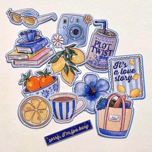 May include: A collection of die-cut stickers featuring blue and yellow illustrations including sunglasses, a camera, books, lemons, a soda can labelled Plot Twist, a bowl of oranges, a blue flower, a striped mug, a tote bag, and a sign saying sorry, I'm too busy.