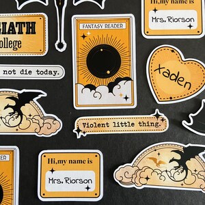 Peut inclure: Une collection d'autocollants d&eacute;coup&eacute;s aux motifs jaunes et noirs. Les &eacute;l&eacute;ments incluent une silhouette de dragon noir, une carte &eacute;tiquet&eacute;e Fantasy Reader, un c&oelig;ur avec le nom Xaden et des &eacute;tiquettes portant Hi, my name is Mrs. Riorson.
