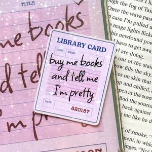 May include: A rectangular sticker designed as a library card with a light purple background and white star accents. The text reads LIBRARY CARD, buy me books and tell me I'm pretty, and the number 820187. It features a dark blue border.