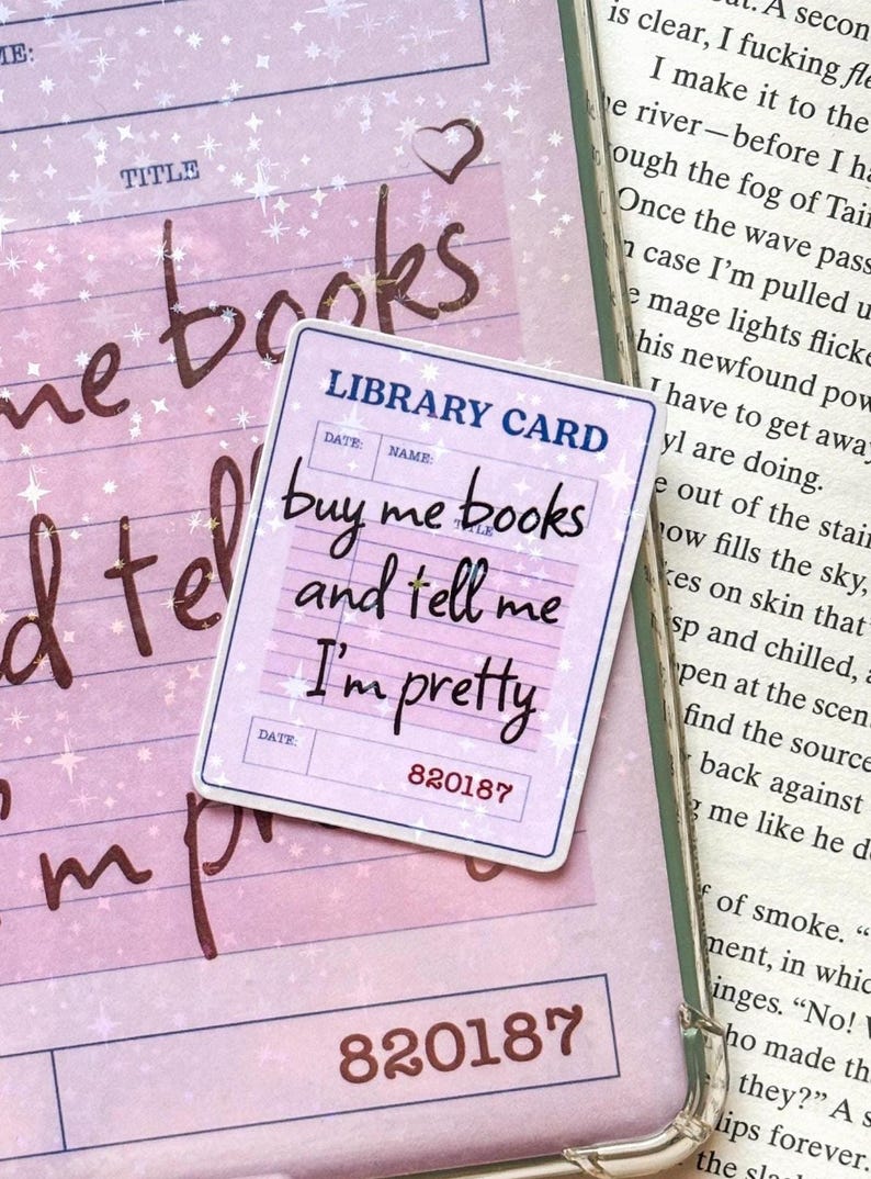 May include: A rectangular sticker designed as a library card with a light purple background and white star accents. The text reads LIBRARY CARD, buy me books and tell me I'm pretty, and the number 820187. It features a dark blue border.