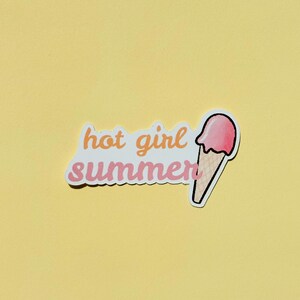 May include: A die-cut sticker featuring the text hot girl summer in a cursive orange and pink font, accompanied by a graphic of a pink ice cream scoop on a tan waffle cone. The design has a white border and is presented on a solid yellow background.