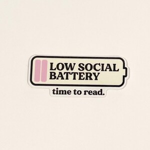 Pu&ograve; includere: Un adesivo bianco con un contorno nero di una batteria con barre rosa all'interno. Il testo "LOW SOCIAL BATTERY" &egrave; stampato in nero sulla batteria. Sotto la batteria c'&egrave; il testo "time to read."