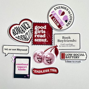 Può includere: Un set di nove adesivi con vari design a tema libro. Gli adesivi sono bianchi con accenti rossi e rosa. Alcuni degli adesivi presentano testo, tra cui "Romance Book Club", "Good Girls Read Smut", "Enemies to Lovers Book Club", "Book Boyfriends: God's apology for men in real life", "Low Social Battery: Time to Read", "Lol, ur not Rhysand", "Emotional Support Kindle" e "Endless TBR".