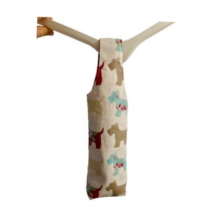 Peut inclure: Un sac à vin en tissu beige avec une poignée. Le sac est décoré d'un motif répété de chiens bruns, bleus et rouges.