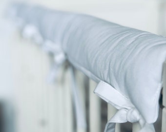 May include: White padded cot rail cover with white ties. The cover is made of soft fabric and is designed to protect babies from bumps and bruises.