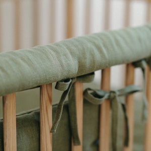 May include: A green linen crib bumper with ties to attach to the crib rails. The bumper is made of soft, natural fabric and is designed to protect babies from bumps and bruises.