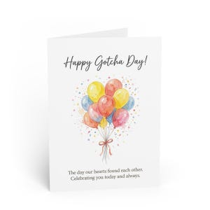 May include: A white greeting card with the text "Happy Gotcha Day!" in a script font. The card features a watercolor illustration of colorful balloons tied with a brown ribbon. The text "The day our hearts found each other. Celebrating you today and always." is below the balloons.