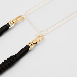 May include: A black braided phone strap with gold clasps attached to a clear phone case.
