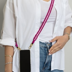 May include: A white button-down shirt with a pink phone strap and a clear phone case with a black screen.