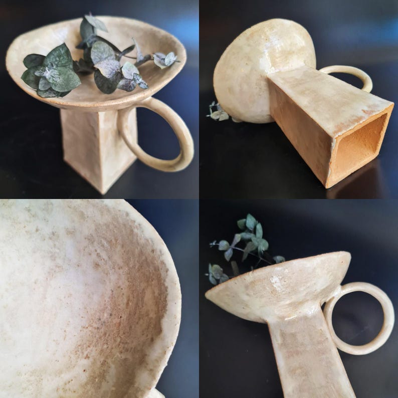 Puede incluir: Un jarr&oacute;n de cer&aacute;mica beige hecho a mano con base cuadrada, tallo cil&iacute;ndrico y asa circular. La parte superior es un plato poco profundo, que contiene ramitas de follaje verde. El jarr&oacute;n tiene una superficie texturizada y un dise&ntilde;o art&iacute;stico &uacute;nico.