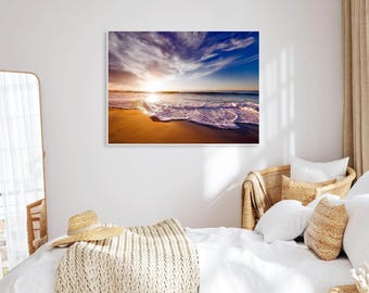 May include: A photograph of a beach scene with a sunset in the background. The waves are crashing on the shore and the sand is golden.