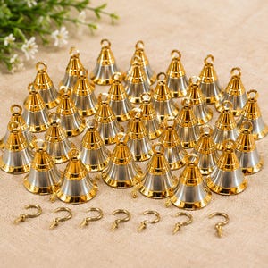 Puede incluir: Una colección de pequeñas campanas de metal en forma de cono con una parte superior dorada brillante y una base plateada. Cada campana tiene un pequeño lazo en el vértice para colgar. Siete ganchos de tornillo dorados están alineados debajo.