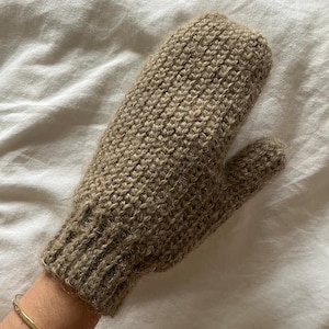 以下が含まれることがあります： 茶色のニットの手袋で、質感のある模様が施されています。手袋は柔らかくふわふわした糸でできています。