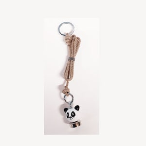 Peut inclure: Un aimant en forme de panda blanc avec un visage et des yeux noirs, attaché à une corde brune avec un anneau argenté.