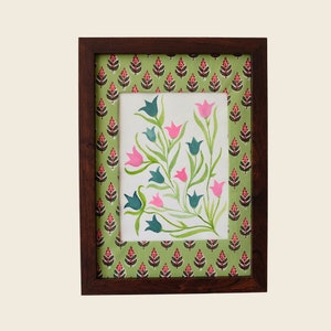 以下が含まれることがあります： 白い背景にピンクとブルーの花と緑の葉を描いた水彩画の額縁。フレームはダークウッド製で、緑とピンクのパターンが施された縁取りが施されています。