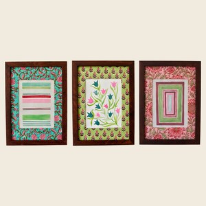 以下が含まれることがあります： 異なるデザインの額装されたプリントが3つあります。左側のプリントは、白地に緑とピンクのストライプが入った、ターコイズブルーとピンクのパターンで縁取られています。中央のプリントは、白地にピンクと緑の花柄が入った、緑とピンクのパターンで縁取られています。右側のプリントは、白地にピンクと緑の幾何学模様が入った、ピンクと赤のパターンで縁取られています。