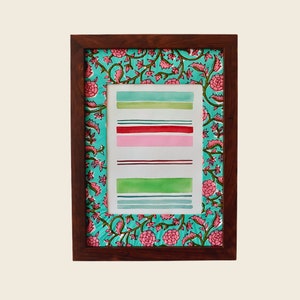 以下が含まれることがあります： 花柄の縁取りが施された額縁に入った水彩画。絵画は緑、ピンク、赤の色合いの水平なストライプが並んでいます。