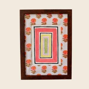 以下が含まれることがあります： 白い背景にピンク、イエロー、グリーンの幾何学模様が描かれた額装されたアート作品。枠には花柄の模様が施されています。