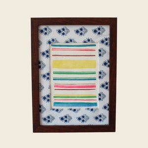 以下が含まれることがあります： 白い背景にカラフルな水平ストライプが描かれた水彩画の額縁。フレームはダークウッド製で、青と白の花柄が施されています。