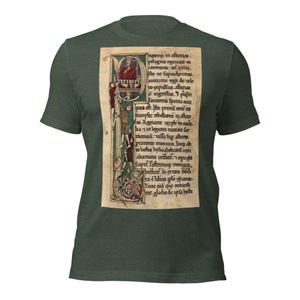 May include: Dark green t-shirt featuring a medieval manuscript design. The manuscript is in a rectangular shape with ornate borders, illustrations, and text. The text is in a script font, and the illustrations include figures and decorative elements.