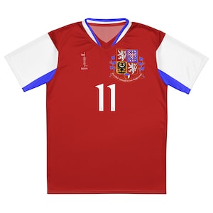 May include: Red soccer jersey with white and blue accents. The jersey has a crest with a coat of arms and the text "Ceska druzstva kopane" and the number "11" on the front.