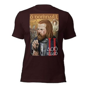 Op de afbeelding: Een maroon t-shirt met een grafische print van een man met een baard en een kroon. De tekst op het shirt luidt "Ó Domhnaill II Aodh Ruadh".