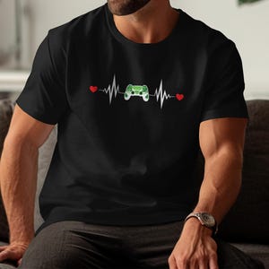 Puede incluir: Camiseta negra con un gráfico de latido cardíaco blanco, corazones rojos y un mando de videojuegos verde. El diseño es un guiño lúdico a la cultura del juego. La camiseta está hecha de un material suave y cómodo.