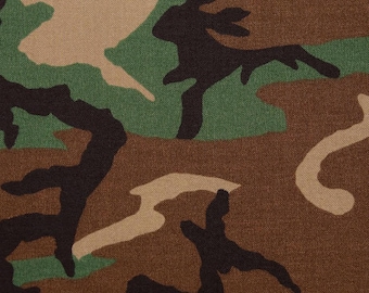 May include: Close-up of a camouflage fabric pattern. The design features irregular shapes in shades of brown, green, tan, and black. The fabric has a textured appearance, suggesting a durable material suitable for outdoor wear or military-inspired items.