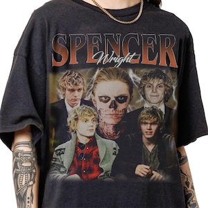 May include: Black t-shirt featuring a graphic design with the text "SPENCER Wright" in orange and white. The design includes multiple images of a person, including one with skull makeup and lightning bolts.