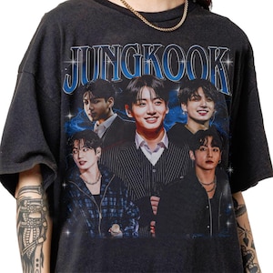 May include: Dark gray t-shirt featuring the name "JUNGKOOK" in blue, with a vintage-style design. The shirt displays multiple images of a person, with a blue and white background.