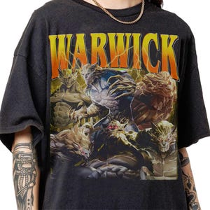 May include: Dark gray t-shirt featuring the word "WARWICK" in orange and yellow, with a lightning bolt design. The shirt displays a graphic of several muscular, humanoid creatures with glowing red eyes.