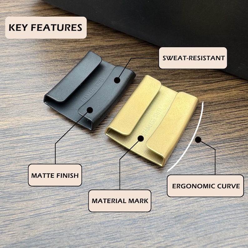 May include: Two rectangular stainless steel keepers with a matte finish, one black and one gold. Each piece features an ergonomic curve and is labeled with the text STAINLESS STEEL. Text labels indicate key features: KEY FEATURES, SWEAT-RESISTANT, MATTE FINISH, MATERIAL MARK, and ERGONOMIC CURVE.