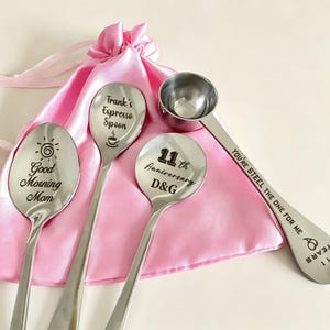 May include: Four stainless steel spoons with engraved text and designs. One spoon says "Good Morning Mom", another "Frank's Espresso Spoon", and a third "11th Anniversary D&G". The fourth spoon says "You're Steel The One For Me".