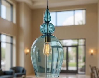 May include: A hanging light fixture with a teal glass shade and a decorative top. The light bulb is visible inside the glass. The fixture is suspended from a black cord in a well-lit room with large windows and a marble floor.