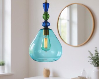 May include: A turquoise glass pendant light with a teardrop-shaped shade. The light fixture has a brass-colored bulb socket and a decorative stem with blue and green glass elements. The light hangs from a black cord.
