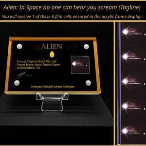 Op de afbeelding: Een ingelijste filmcel uit de film "Alien", met de titel en slogan. De zwarte lijst heeft gouden randen en bevat de filmcel, tekst en een handtekening. De lijst wordt op een transparante standaard gepresenteerd.