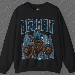 May include: Black sweatshirt with a graphic print of a football player in a blue uniform with the word "DETROIT" in blue letters above the player. The player is surrounded by three lions with flames behind them.
