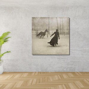 May include: A black and white photograph of a person in a long coat walking away from two horses in a snowy field.