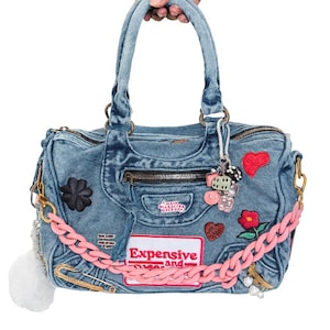 Könnte beinhalten: Hellblaue Jeans-Handtasche mit Patches, Charms und einer rosa Kette. Die Tasche hat einen oberen Griff und einen Reißverschluss. Der Text "Expensive and..." ist auf einem Patch zu sehen.