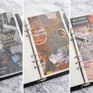 May include: Three open black ring binder planners with lined pages. Each planner has a decorative cover with text and images. The first says "2026 My Year of Winning" and "Luxury Life". The second says "Care For Your Body" and "10,000 steps a day". The third says "My Own Business" and "Everything".