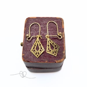 May include: A pair of gold filigree earrings with a diamond shape design. The earrings are in a small red velvet box.
