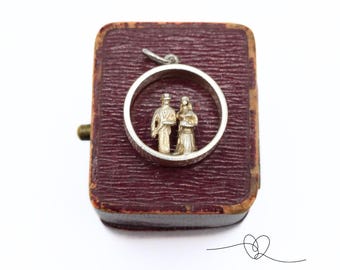 May include: A silver charm in a red velvet box, depicting a bride and groom in a circle.
