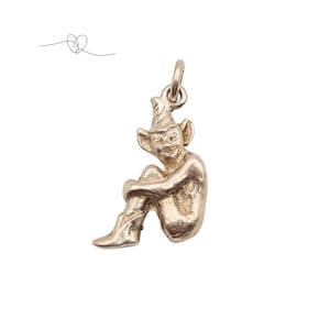 May include: A silver-coloured charm depicting a seated elf with a pointed hat and large ears. The elf is hugging its knees, and the charm has a loop at the top for attaching to a bracelet or necklace. The charm is set against a white background.